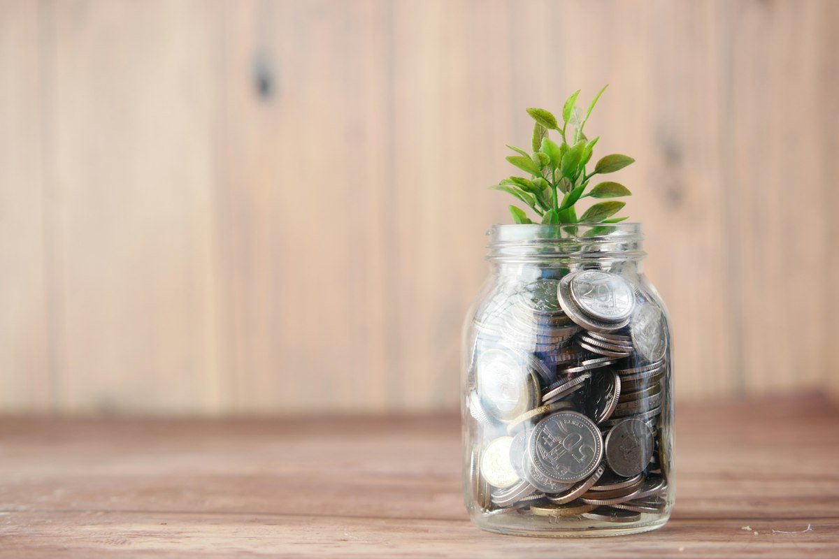 Frasco de vidrio con monedas junto a una planta, ejemplo de apartar dinero en tu presupuesto mensual