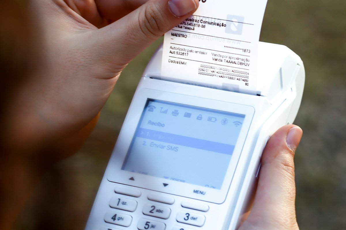 Persona con celular y ticket de compra en mano, donde se ve el IVA que pagas en cada compra