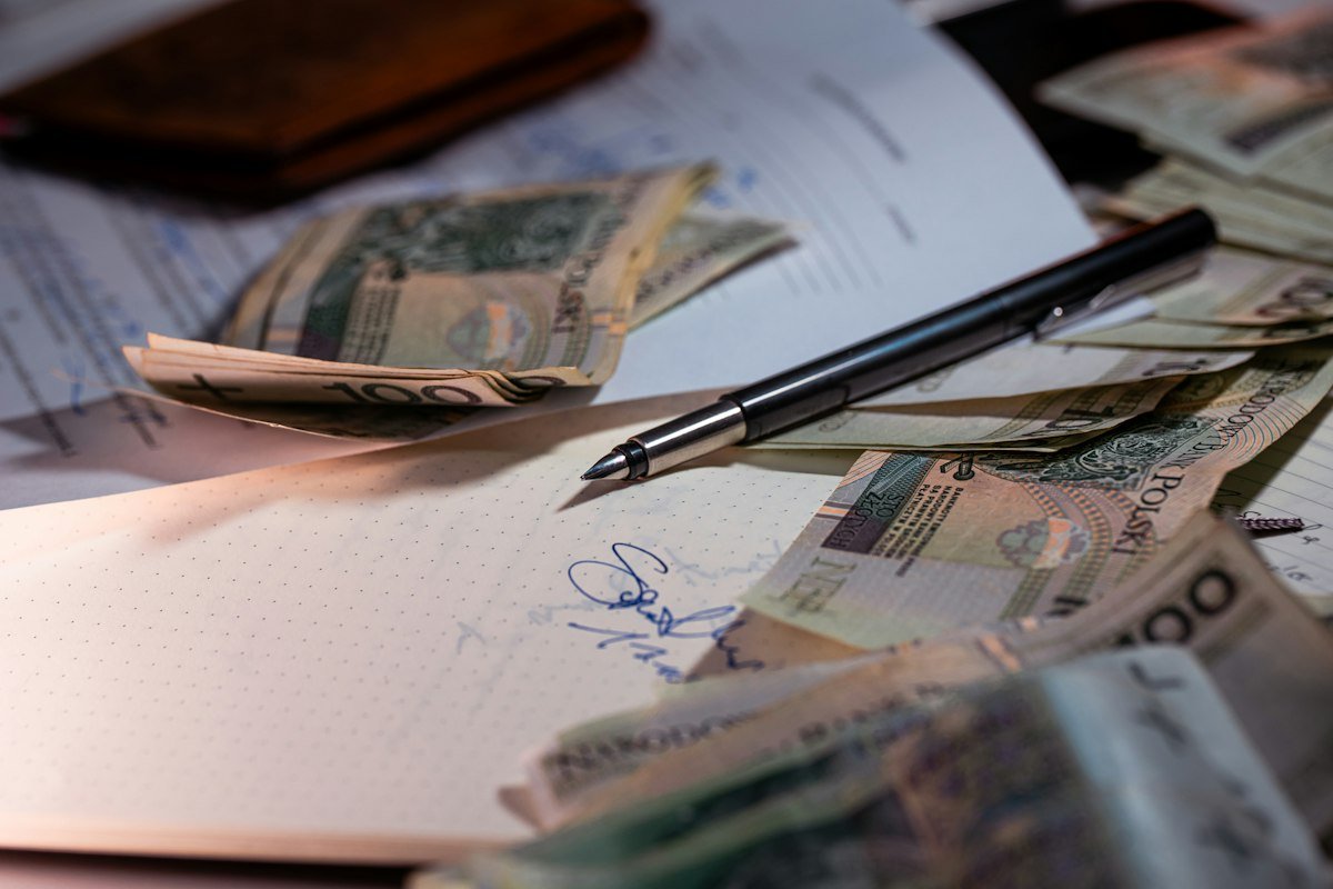 Pluma y dinero sobre documentos financieros, estado de cuenta de una tarjeta y pago mínimo
