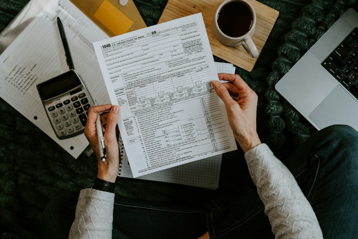 Manos sosteniendo formatos de impuestos junto a una calculadora y una laptop para ordenar comprobantes